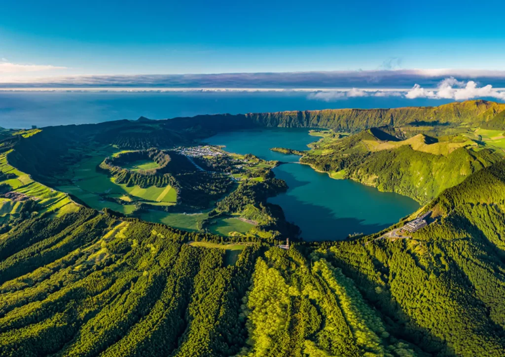 Aerial view of a lush green landscape in the Azores featuring lakes and hills under a clear blue sky.