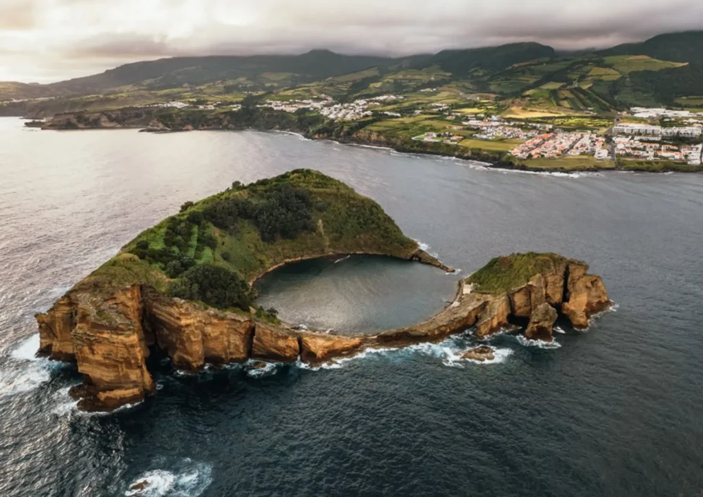 Aerial view of a coastal island with a circular bay surrounded by cliffs in the Azores.