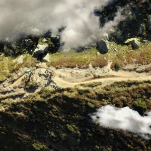 Aerial view of mountain bikers riding along a dirt trail surrounded by rocky terrain and clouds.