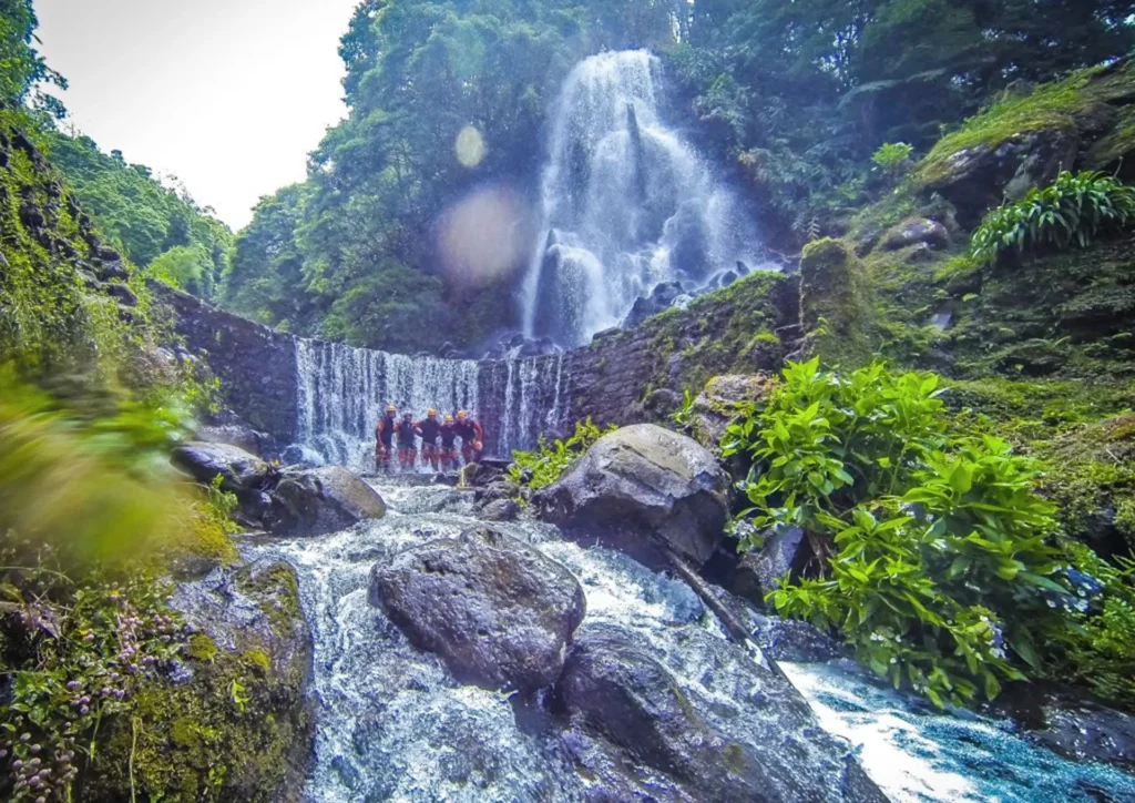 Group of individuals participating in canyoning near a waterfall in Sao Miguel, Azores.