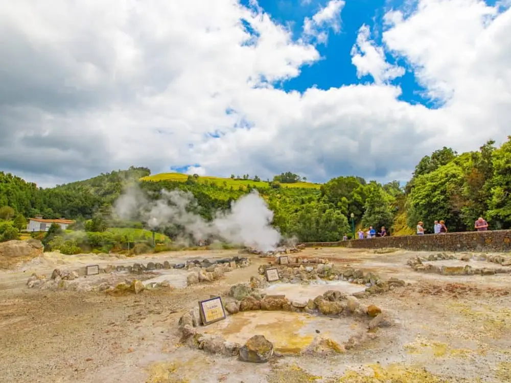 Geothermal area in Furnas with steam rising from hot springs and rocky formations.