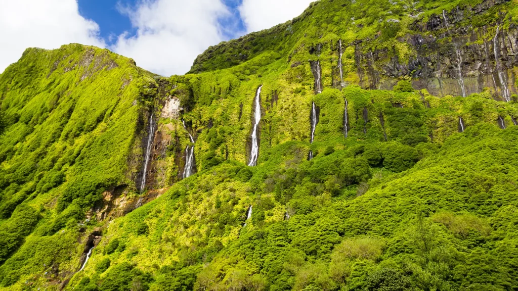A green mountain landscape featuring multiple waterfalls cascading down the rocky surface.