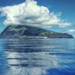 View of Corvo Island with a cloud formation above and reflection in the water.