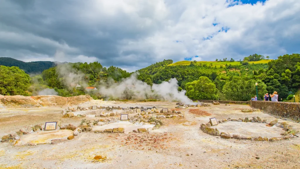 Geothermal area at Furnas Lake with steam rising from the ground and rock formations.