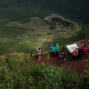 A group of hikers gathered at an overlook with a view of a caldeira and surrounding landscape.