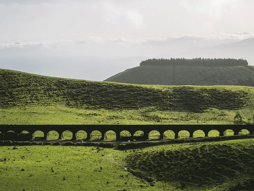 Aqueduct structure with multiple arches set against a green landscape in Sete Cidades.