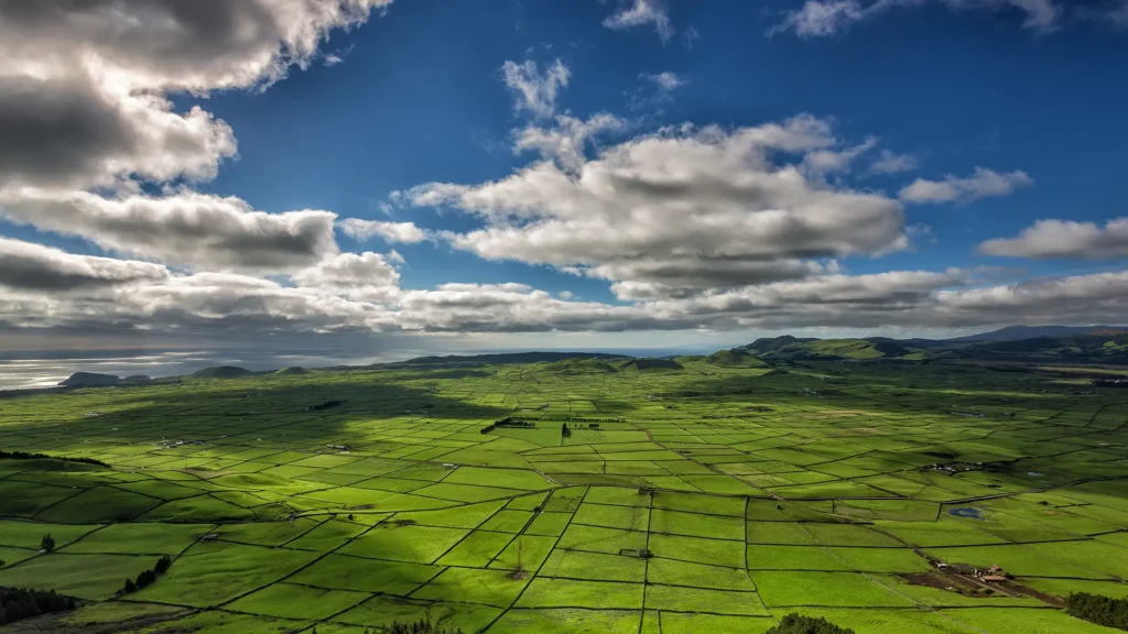 Expansive green landscape featuring fields and a cloudy sky over a hilly terrain.