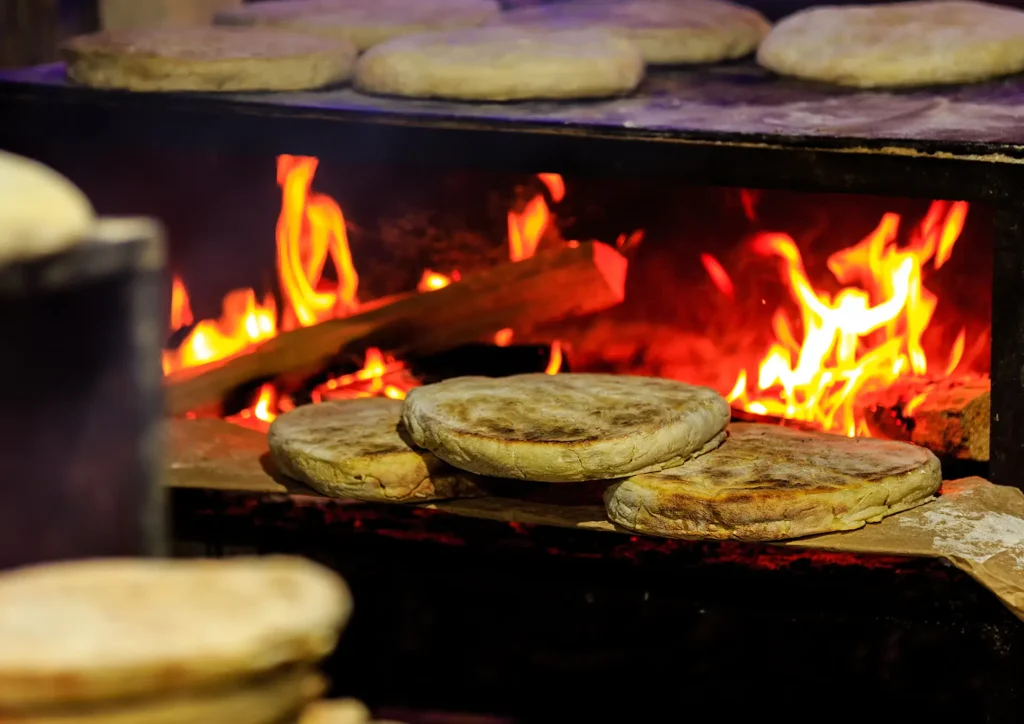 Flatbreads baking on a wooden surface above an open flame in a traditional setting.