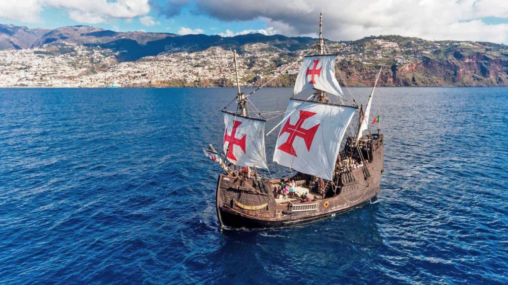 A replica of the Santa Maria ship sailing on the ocean with sails displaying red crosses.