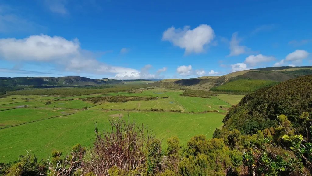 Expansive green landscape featuring rolling hills and a clear blue sky with scattered clouds.