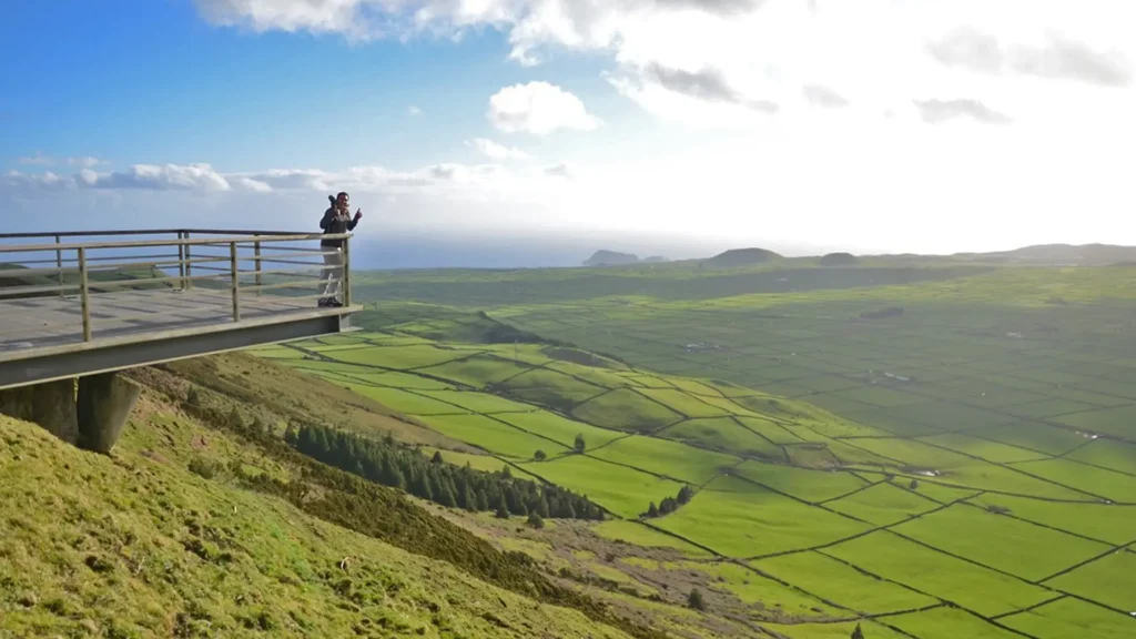 Person standing on a viewpoint overlooking green fields and hills on Terceira Island.