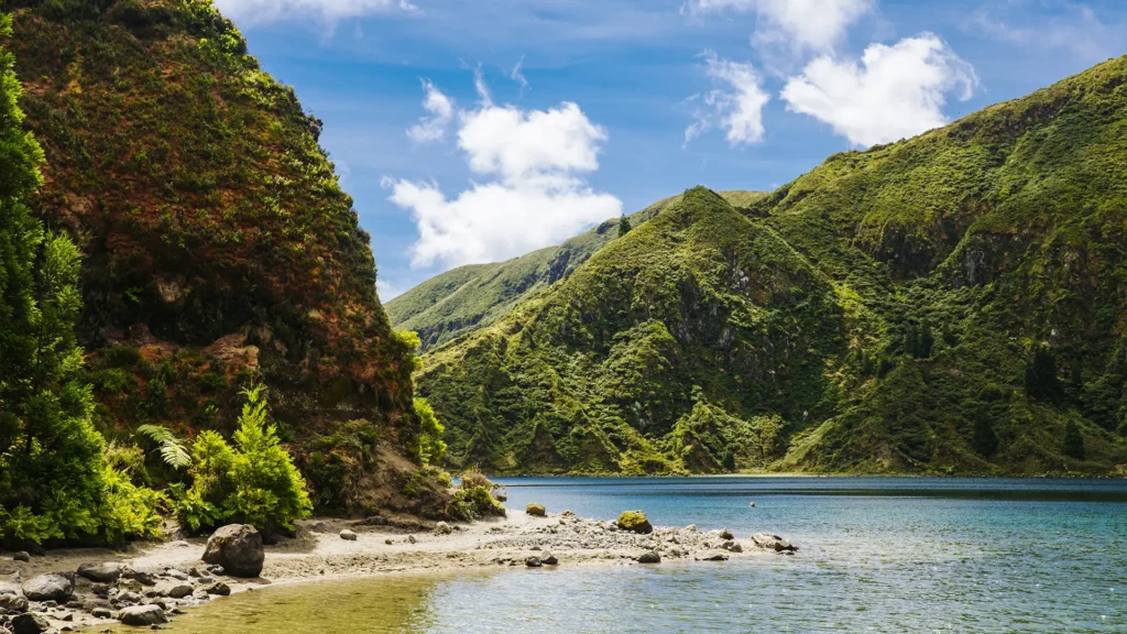 Scenic view of Lagoa do Fogo with green hills and calm water under a blue sky.