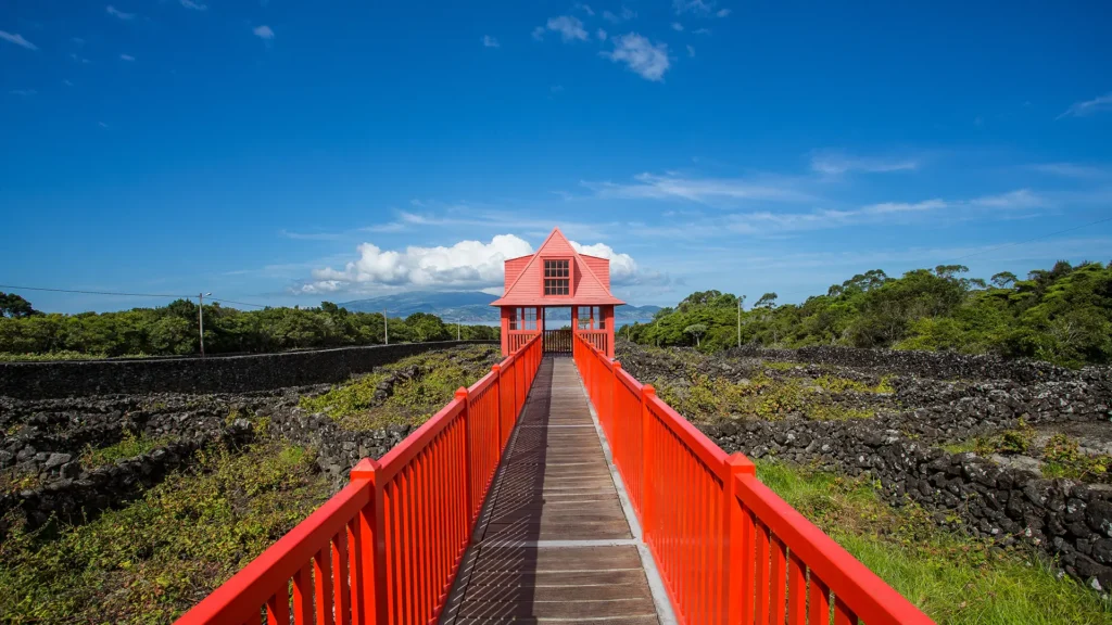 A red bridge connecting to a building with a peaked roof against a blue sky.