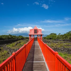 A red bridge connecting to a building with a peaked roof against a blue sky.