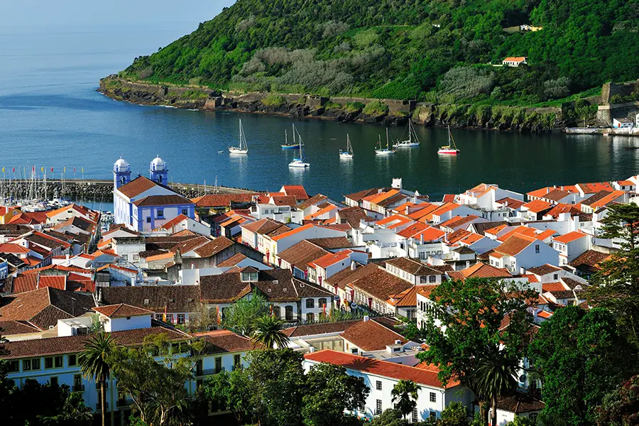 Aerial view of Terceira Island featuring red-tiled roofs and a calm bay with boats.